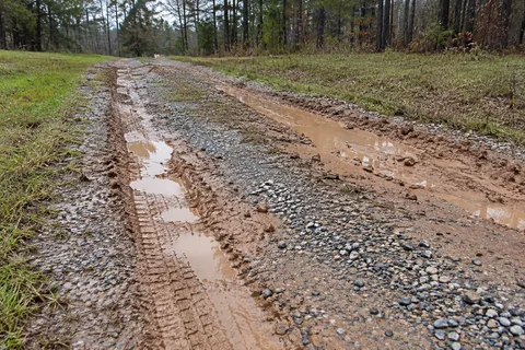 Deep muddy tire ruts holding water on a gravel drive
