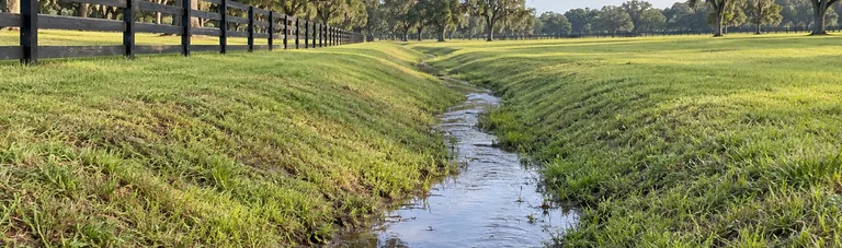 Finished grassy drainage swale carrying water through a horse farm